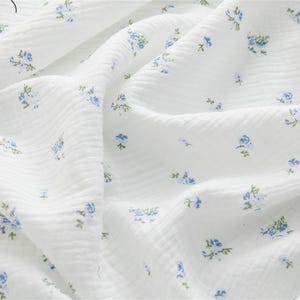 May include: White cotton fabric with a subtle texture and a small blue floral pattern.