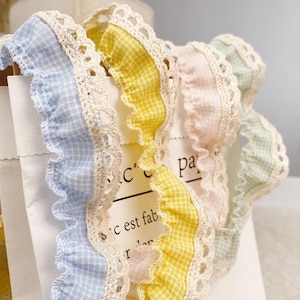 Può includere: Primo piano di nastri a quadretti dai colori pastello con un bordo in pizzo smerlato. I nastri sono nelle tonalità di blu, giallo, rosa e verde. Il testo "c est fab" è parzialmente visibile.