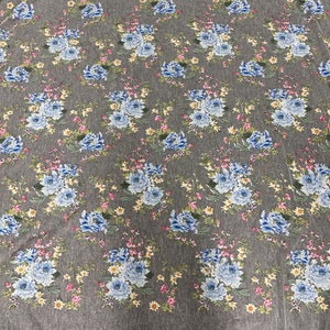 Puede incluir: Tela de tul blanco con estampado floral con flores azules, rosas y amarillas. La tela tiene una textura delicada y transparente.