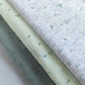 Pu&ograve; includere: Primo piano di tre tessuti diversi con una trama a coste. I tessuti sono in tonalit&agrave; di verde e bianco, con un delicato motivo floreale. I tessuti sono sovrapposti.