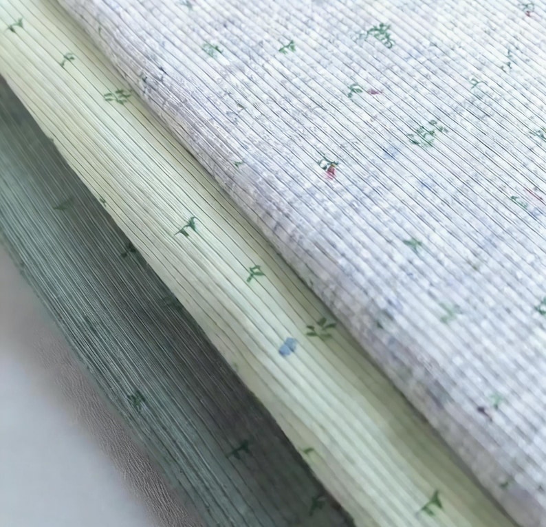Pu&ograve; includere: Primo piano di tre tessuti diversi con una trama a coste. I tessuti sono in tonalit&agrave; di verde e bianco, con un delicato motivo floreale. I tessuti sono sovrapposti.
