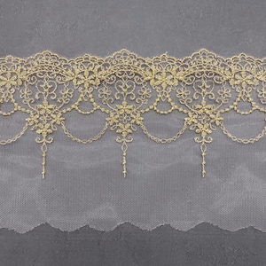May include: Gold lace trim with a delicate floral pattern and a scalloped edge. The lace is on a sheer white mesh background.