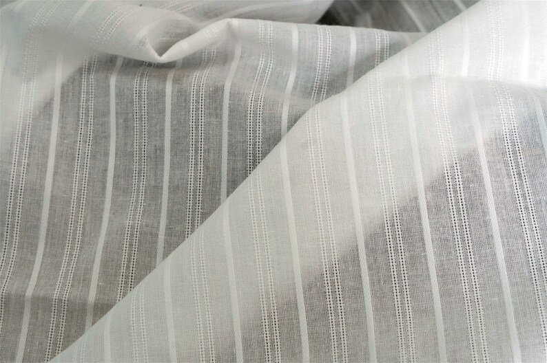 May include: White sheer fabric with thin vertical stripes. The fabric is woven with a subtle texture.