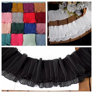 Puede incluir: Una colección de tiras de tela plisada disponibles en una amplia variedad de colores sólidos, incluyendo negro, blanco, rojo, azul, verde, rosa y amarillo. Cada tira presenta una textura plisada tipo acordeón con un borde con volantes.