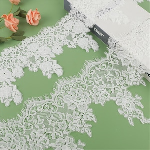 May include: White lace trim with a scalloped edge and floral pattern. The lace is delicate and intricate, with a soft, flowing texture.