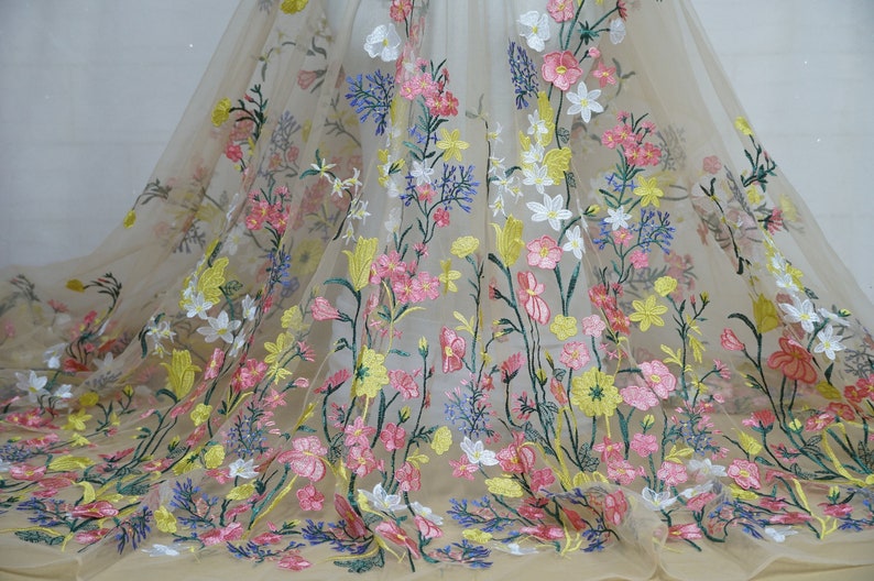 May include: Beige tulle fabric with embroidered floral designs in pink, yellow, white, and green.