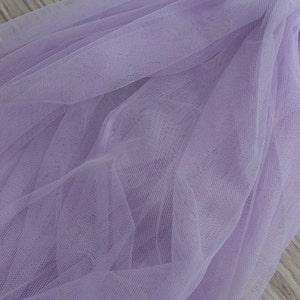 Puede incluir: Primer plano de una tela de tul suave y de color lila claro, con una textura de malla fina y delicada.