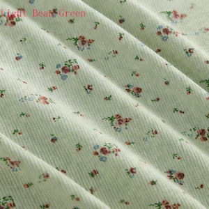 Pu&ograve; includere: Tessuto a coste verde chiaro con motivo floreale. Il tessuto presenta piccoli gruppi di fiori rossi, blu e verdi, sparsi sulla superficie. Il testo "Light Bean Green" &egrave; visibile nell'angolo in alto a sinistra.