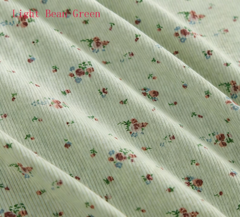 Pu&ograve; includere: Tessuto a coste verde chiaro con motivo floreale. Il tessuto presenta piccoli gruppi di fiori rossi, blu e verdi, sparsi sulla superficie. Il testo "Light Bean Green" &egrave; visibile nell'angolo in alto a sinistra.