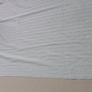 May include: White cotton fabric with a delicate eyelet pattern. The fabric has vertical rows of small holes, creating a lacy effect. The edges of the fabric are scalloped.