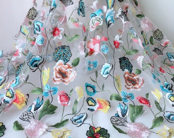May include: White sheer fabric with colorful embroidered flowers. The flowers are in shades of pink, blue, yellow, green, and red.