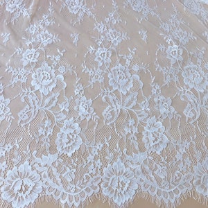 May include: White floral lace fabric with a delicate pattern. The lace has a scalloped edge and is perfect for crafting, sewing, or adding a touch of elegance to any project.