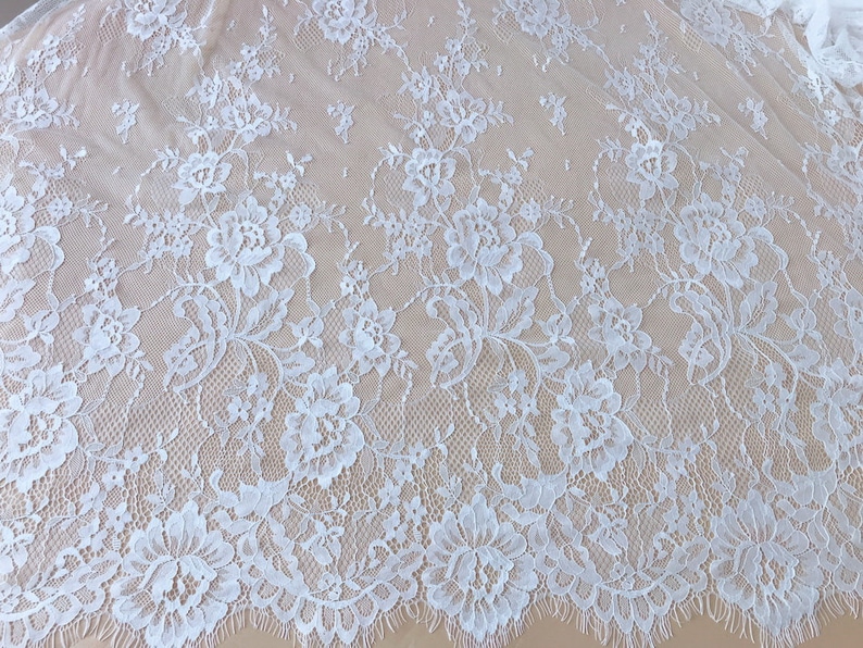 May include: White floral lace fabric with a delicate pattern. The lace has a scalloped edge and is perfect for crafting, sewing, or adding a touch of elegance to any project.