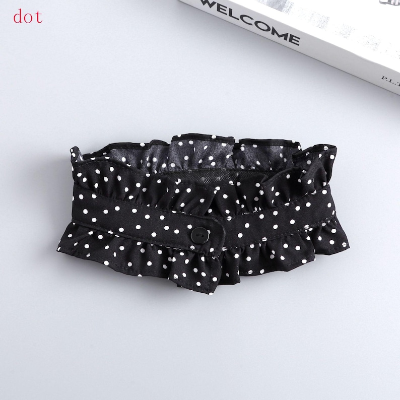 May include: Black and white polka dot ruffled collar with a button closure. The collar is made of a soft fabric and has a delicate, feminine design. The word "dot" is in the top left corner.