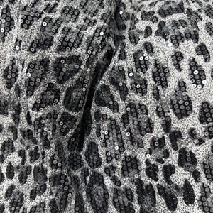 Puede incluir: Primer plano de una tela con diseño de estampado de leopardo. La tela está cubierta de pequeñas lentejuelas brillantes en tonos grises y negros, creando una apariencia texturizada y glamurosa. El patrón es un estampado animal clásico.