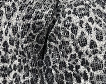 Puede incluir: Primer plano de una tela con diseño de estampado de leopardo. La tela está cubierta de pequeñas lentejuelas brillantes en tonos grises y negros, creando una apariencia texturizada y glamurosa. El patrón es un estampado animal clásico.
