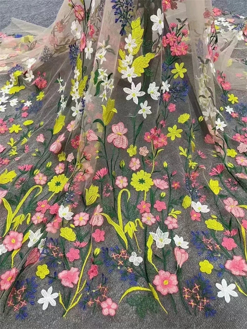 May include: A sheer fabric with embroidered floral designs in shades of pink, yellow, green, and blue. The flowers are various sizes and shapes, creating a delicate and intricate pattern.
