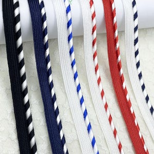 Könnte beinhalten: Nahaufnahme verschiedener bunter Kordeln. Die Kordeln sind in den Farben Schwarz, Marineblau, Weiß, Rot und Blau gehalten. Einige Kordeln haben eine einfarbige Farbe, andere ein gestreiftes Muster. Die Kordeln sind vertikal nebeneinander angeordnet.