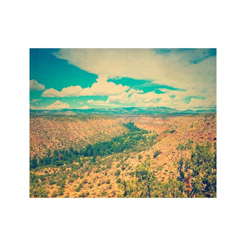 May include: A scenic view of a canyon with a winding river running through it. The canyon walls are a mix of brown and green, and the sky is a bright blue with fluffy white clouds.