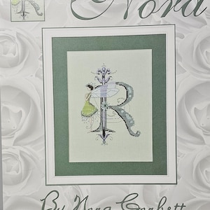 May include: Cross stitch pattern featuring a fairy with wings and a green dress standing next to the letter R. The pattern is titled "Letters From Nora" and is designed by Nora Corbett.
