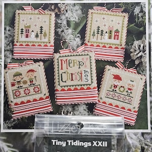 May include: A collection of five cross-stitch Christmas ornaments with red and white striped borders. Each ornament features a different holiday scene, including houses, trees, and figures. The top of the image displays the text "Lizzie Kate". A small embellishment pack is visible at the bottom.
