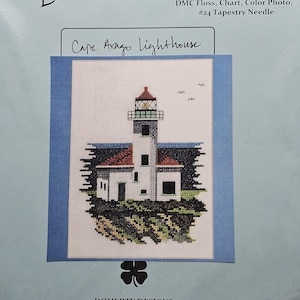 May include: A counted cross-stitch kit by Doherty Designs featuring a Cape Arago Lighthouse design. The kit includes 100% cotton 14-count Aida cloth, DMC floss, a chart, color photo, and a #24 tapestry needle. The lighthouse is white with a red roof and sits on a green and brown landscape.