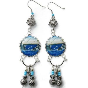 May include: A pair of dangle earrings featuring a seascape design. The earrings have a silver-tone metal construction with a blue and white ocean scene. They include decorative beads and a floral accent near the ear hook.