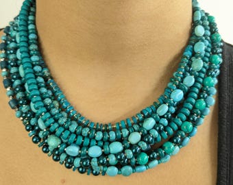May include: A multi-strand necklace made of turquoise and green beads. The necklace is layered and has a variety of bead sizes and shapes.