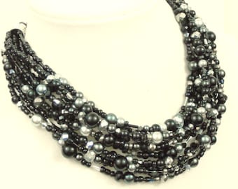May include: Multi-strand necklace with black, silver, and gray beads. The necklace is made of various sizes and shapes of beads, including round, oval, and faceted beads.