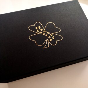 May include: A black box with a gold four-leaf clover design and the text "Mr. Gogo Puzzles" printed on it.