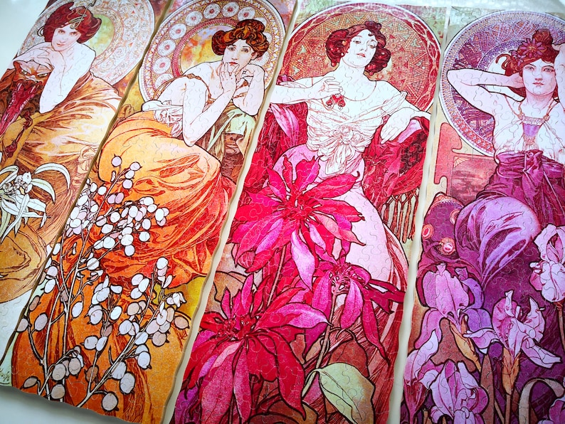 May include: Four panels of a jigsaw puzzle featuring Art Nouveau style illustrations of women with floral accents. The panels feature a woman in a flowing orange dress, a woman in a pink dress, a woman in a purple dress, and a woman in a red dress. The panels are all connected and show a variety of flowers, including lilies, roses, and irises.