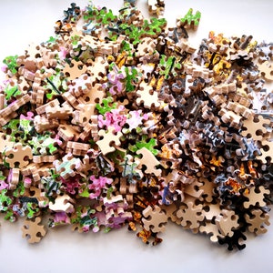 May include: A pile of colorful jigsaw puzzle pieces, with a variety of floral and abstract designs. The pieces are made of wood and have a light brown color.