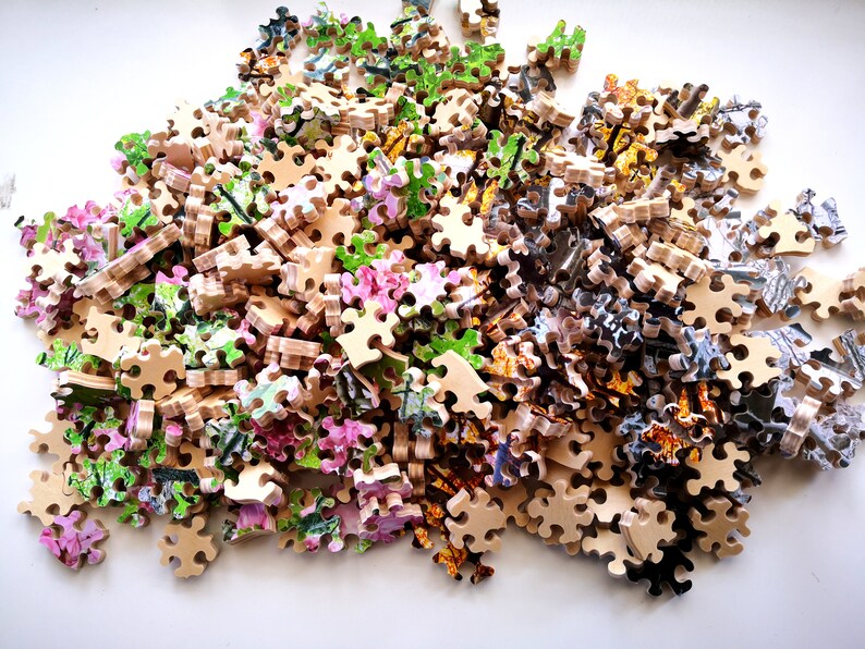 May include: A pile of colorful jigsaw puzzle pieces, with a variety of floral and abstract designs. The pieces are made of wood and have a light brown color.