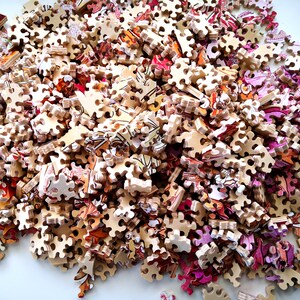 May include: A pile of colorful jigsaw puzzle pieces, mostly brown with some pink and orange accents. The pieces are scattered on a white surface.