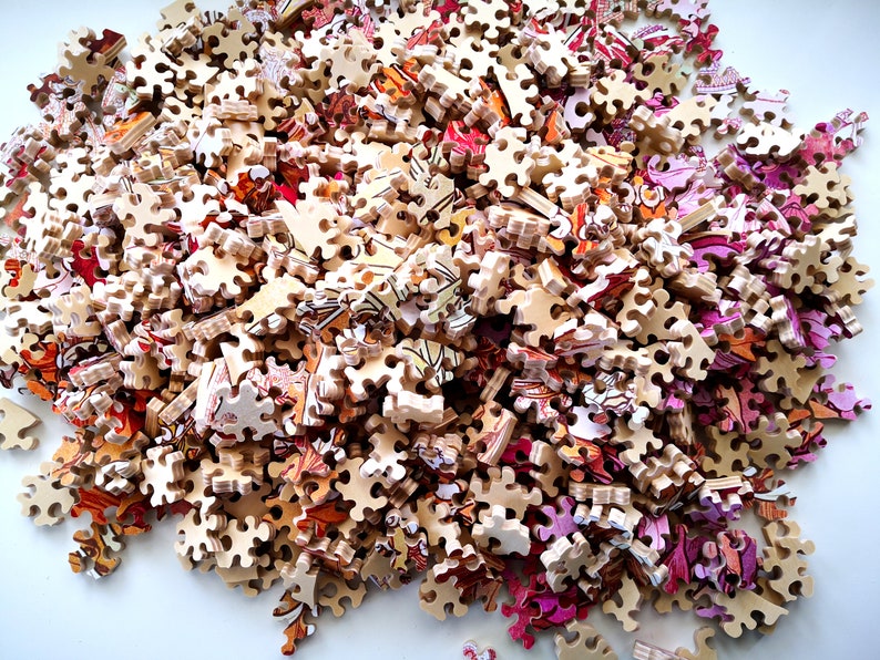 May include: A pile of colorful jigsaw puzzle pieces, mostly brown with some pink and orange accents. The pieces are scattered on a white surface.