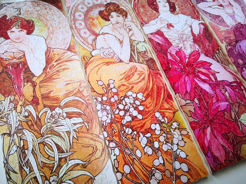 May include: Four jigsaw puzzle pieces featuring Art Nouveau style illustrations of women in elaborate dresses and floral designs. The pieces are arranged in a row, with the women's faces visible in each piece. The colors are vibrant and include shades of orange, pink, red, and white.