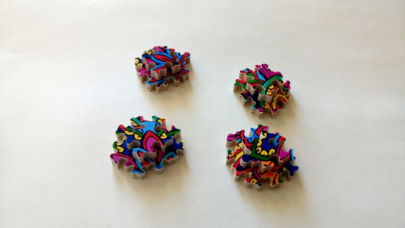 Peut inclure: Quatre piles de pi&egrave;ces de puzzle color&eacute;es avec des motifs complexes. Chaque pile est compos&eacute;e de plusieurs pi&egrave;ces, cr&eacute;ant un effet de superposition. Les pi&egrave;ces sont dispos&eacute;es en forme carr&eacute;e, chaque pile &eacute;tant l&eacute;g&egrave;rement d&eacute;cal&eacute;e par rapport &agrave; la suivante.