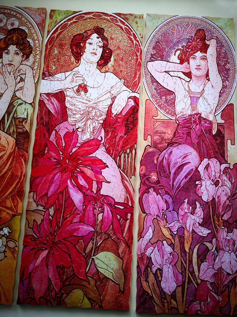 May include: Three panels of a vintage art nouveau style jigsaw puzzle featuring three women in elaborate dresses and floral designs. The women are depicted with long flowing hair and delicate features. The floral designs are intricate and colorful, with shades of pink, red, and purple.