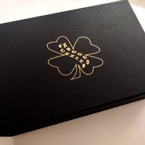 May include: A black box with a gold four-leaf clover design and the text "Mr. Gogo Puzzles" printed on it.