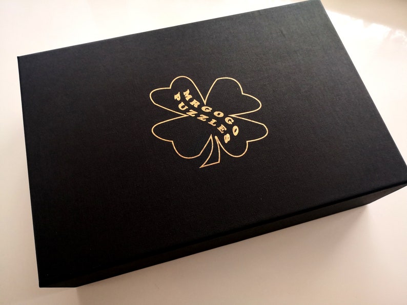 May include: A black box with a gold four-leaf clover design and the text "Mr. Gogo Puzzles" printed on it.
