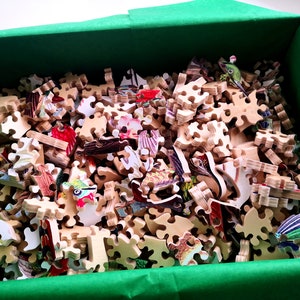 May include: A green box filled with a wooden jigsaw puzzle. The puzzle pieces are scattered and show a variety of colorful images.