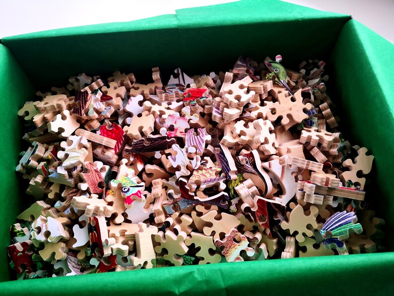 May include: A green box filled with a wooden jigsaw puzzle. The puzzle pieces are scattered and show a variety of colorful images.