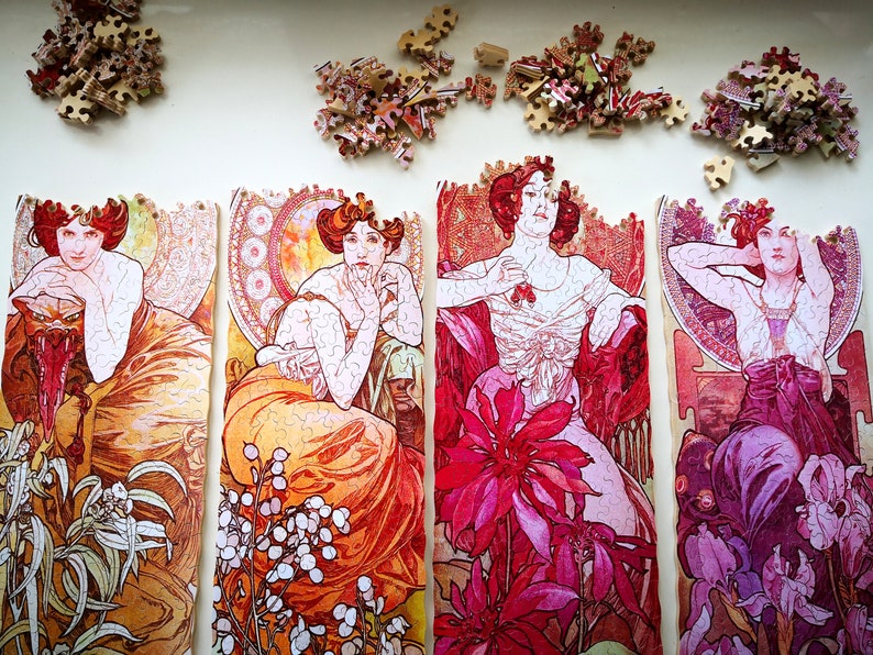 May include: Four jigsaw puzzle pieces featuring Art Nouveau style illustrations of women in elaborate dresses and floral designs. The pieces are in various shades of pink, red, orange, and purple.