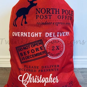 May include: Red Christmas gift sack with a black reindeer silhouette and the words "North Pole Post Office" and "Overnight Delivery." The sack includes the name "Christopher" in white script and a "Do Not Open Before 25 December" stamp.