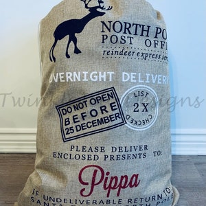 May include: A large beige burlap Santa sack with black and burgundy text and a reindeer silhouette. Text includes "North Pole Post Office," "Overnight Delivery," "Do Not Open Before 25 December," and "Pippa."