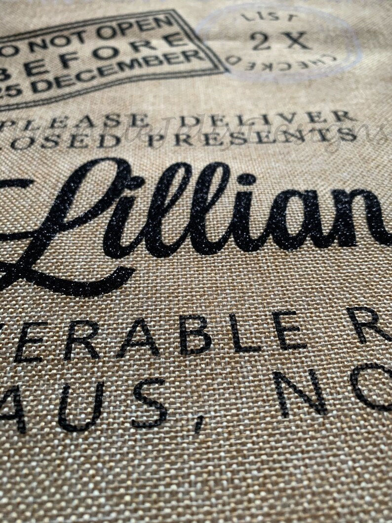 May include: Close-up of a burlap fabric with black text. The text includes the name "Lillian" in a cursive font, along with phrases like "Do Not Open Before 25 December" and "Please Deliver Closed Presents."