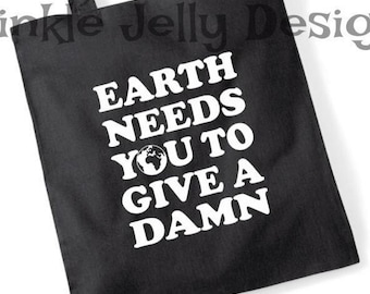 May include: Black tote bag with white text that reads "EARTH NEEDS YOU TO GIVE A DAMN" with a globe graphic. The bag has two black handles and is made of a sturdy fabric.