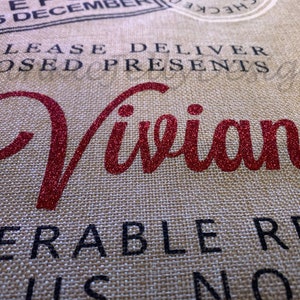 May include: Close-up of a burlap fabric with the name "Vivian" in red glitter script. The text "PLEASE DELIVER CLOSED PRESENTS TO" and other phrases are printed in black, with a stamp graphic at the top. The theme is gift delivery.