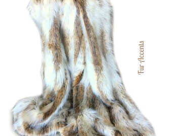 May include: A white and brown faux fur throw blanket with a striped pattern. The blanket is folded and draped over a white surface.