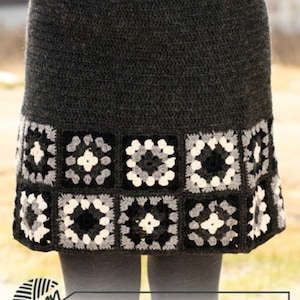 May include: A gray crochet skirt with a black, white, and gray granny square border. The skirt is made with a simple stitch and has a fitted waist. The skirt is shown on a model wearing black tights.
